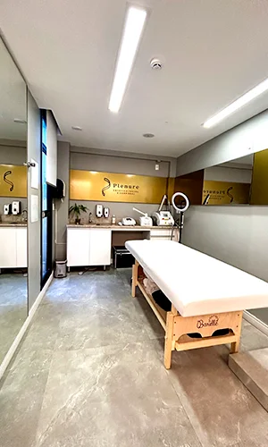 Sala de procedimentos com maca de madeira clara, equipamentos estéticos e painel dourado da Plenure