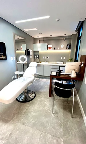 Sala de atendimento com maca branca, bancada com pia e espelho de corpo inteiro